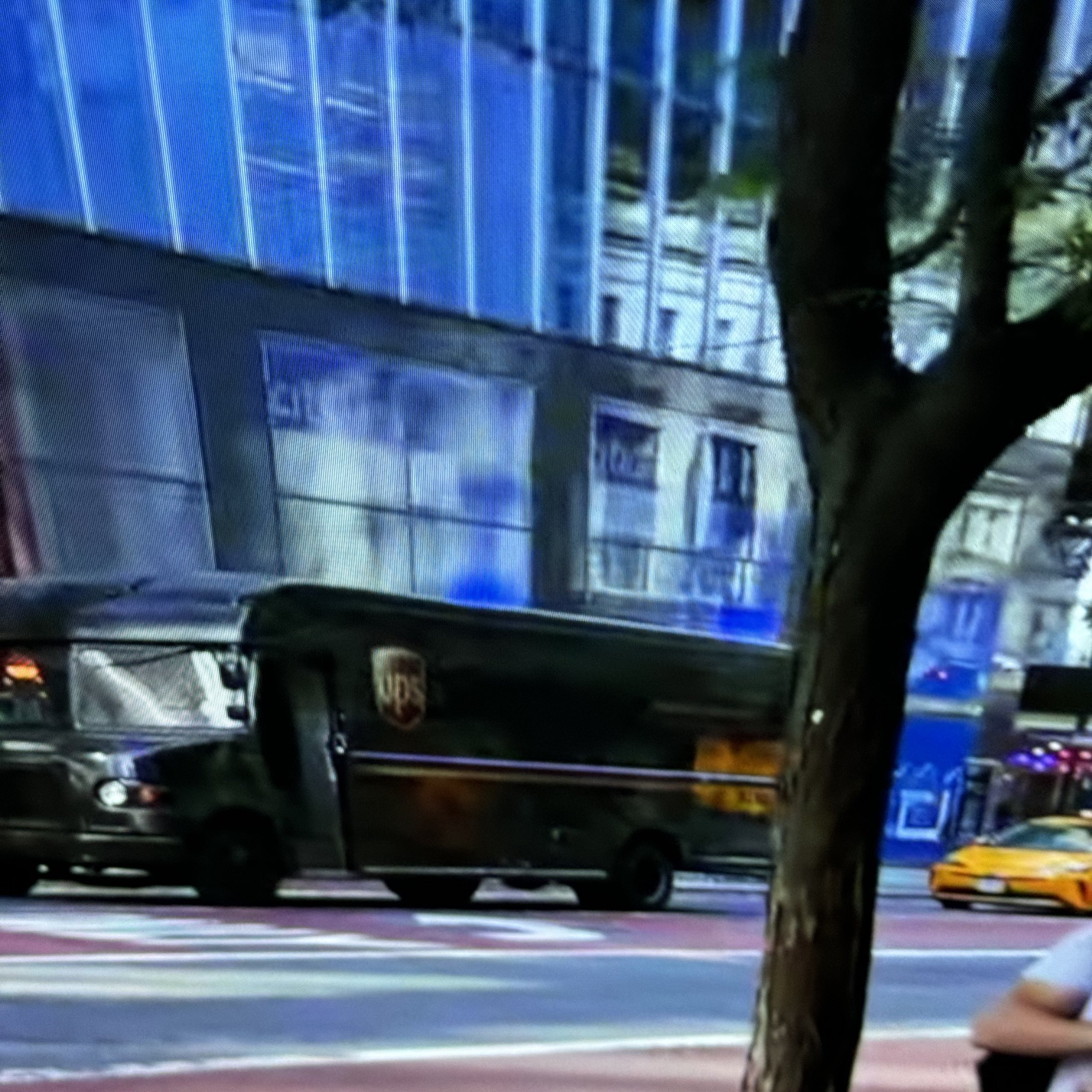 From a screen: brown delivery trucks on a city avenue, a taxi passing